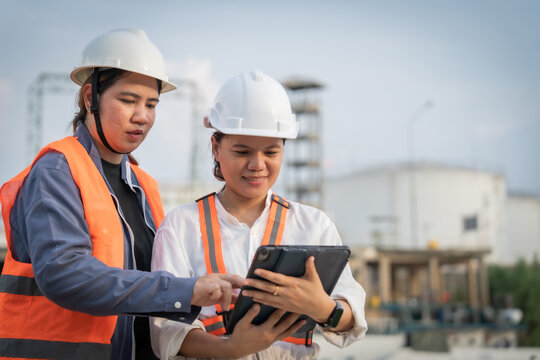 Two engineers in hard hats review data on a tablet. One points, guiding the other through technical details. Their focused expressions show teamwork and precision