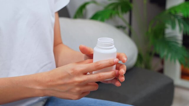 Woman sitting on sofa taking medication from a pill bottle at home, healthcare and treatment concept