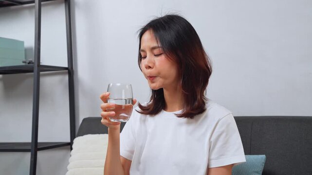 Happy Asian woman drinking a glass of water in the morning at home, healthy lifestyle and wellness concept