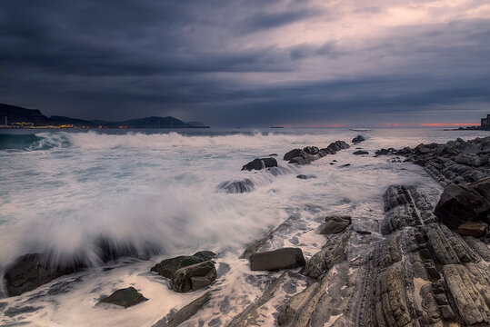 Sunset at Punta Galea Getxo with dramatic orange clouds over a rocky coast and long exposure silk effect on the ocean waves near the port wall