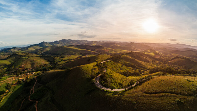 Vista a&eacute;rea de uma estrada sinuosa pelas colinas da Serra da Mantiqueira, Minas Gerais, Brasil, sob a luz dourada do p&ocirc;r do sol.