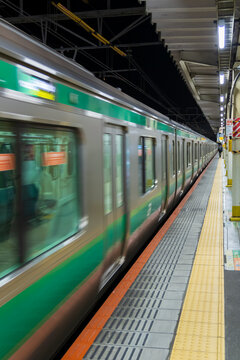 green line commuter train arriving at platform at night in tokyo