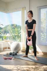 Young woman exercising at home, squat with a kettlebell in a bright and modern living space. Healthy lifestyle and home workout routine concept. © wattana