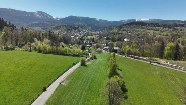 Aerial view of a mountain town with meadows and snow capped peaks of Karkonosze Mountains Poland in spring