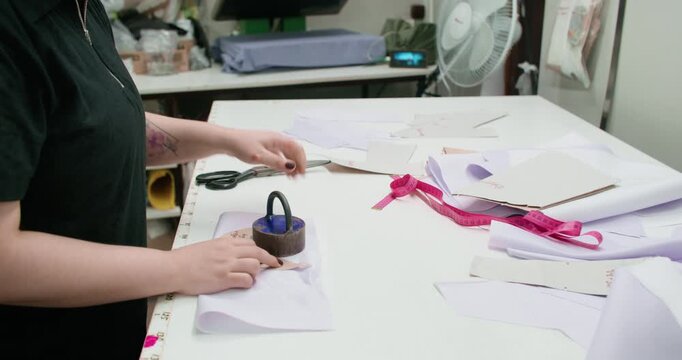 Cutting textile. Atelier work. Woman making pattern with scissors on studio table. Seamstress preparing garment pieces for sewing.