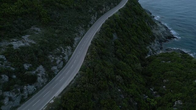 Aerial drone shot of mountain road with car driving along cliff edge above mediterranean sea, Cap Corse, Corsica