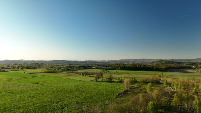 Aerial view of green meadows and fields with forested hills on the horizon at sunrise in spring