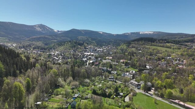 Aerial view of mountain resort town in green valley with snow patches on peaks in spring