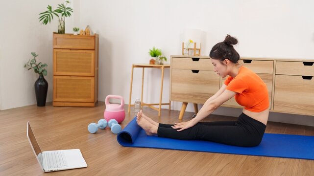 Asian women online fitness workout stretching exercise yoga mat using laptop computer virtual training watching video tutorial health wellness home living room