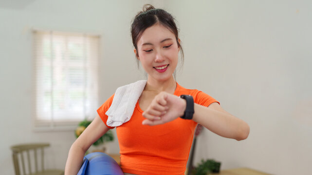 Asian women check smartwatch fitness tracker after workout exercise training at home living room track heart rate calories burned monitor health wellness