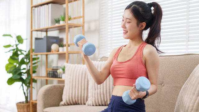 young Asian women doing home workout exercise training lifting dumbbells weights in living room fitness healthy lifestyle strength building bodybuilding