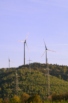 Wind turbines and power lines on a green forested hill under a clear blue sky