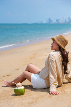 Vertical portrait image of a woman enjoy sitting with a fresh coconut juice on the beach