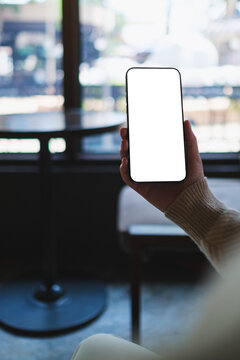 Vertical mockup image of a woman holding and using mobile phone with blank desktop screen in cafe
