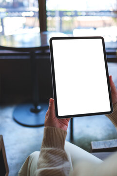 Vertical mockup image of a woman holding digital tablet with blank white desktop screen in cafe