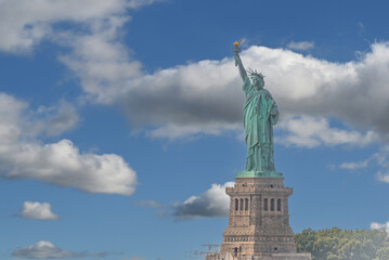 Fototapeta premium New york, usa august 16,2024. Iconic statue of liberty, an american landmark representing democracy and immigration, standing tall against a bright blue sky with clouds