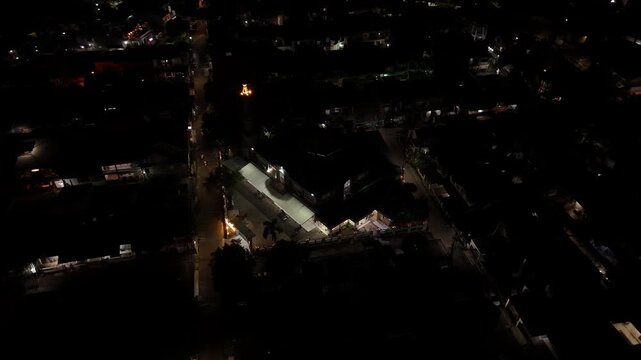Night aerial view rotating over a residential area with a brightly lit building and street lights in Indonesia.