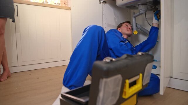 Professional plumber fixing pipes under kitchen sink with toolbox nearby, highlighting repair service, maintenance work, and technical skills
