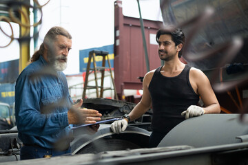Fototapeta premium Two mechanics collaborating on truck maintenance, with a supervisor inspecting the work at an industrial vehicle depot to ensure quality control and safety