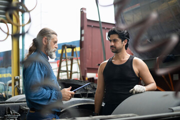 Fototapeta premium Two mechanics collaborating on truck maintenance, with a supervisor inspecting the work at an industrial vehicle depot to ensure quality control and safety