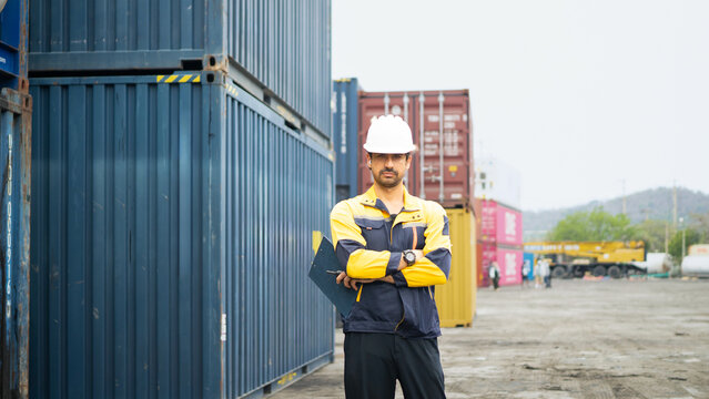 industrial engineer in yellow hard hat and safety vest standing, holds clipboard checking container at container yard warehouse. Shipping import export, Logistics business