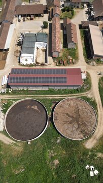 Aerial View of a Rural Farm with Solar Panels: An expansive aerial perspective reveals a working farm with agricultural buildings, silos, and a modern touch with solar panels installed on a barn roof.