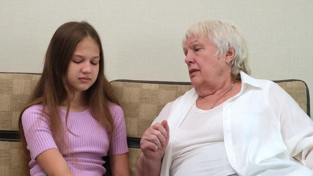 Senior woman scolding and gesturing while teenage girl listens attentively on couch at home. Grandmother scolds her granddaughter indoors. Concept of family communication