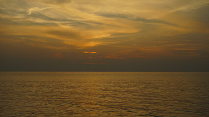 Obraz premium Golden sunset over the ocean with dramatic clouds reflecting warm tones across the water.