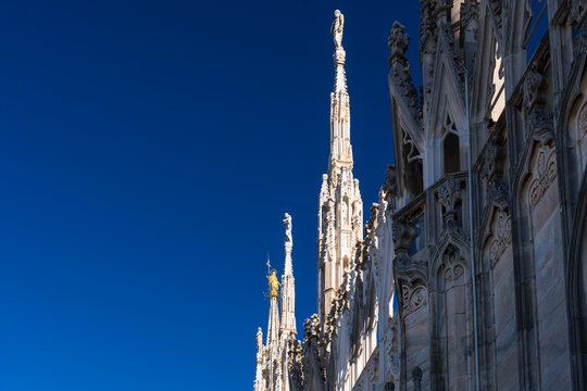 Madonnina golden and marble spiers and statues, architecture on roof of Duomo gothic cathedral in Milan, background blue sky, Lombardy, Italy.