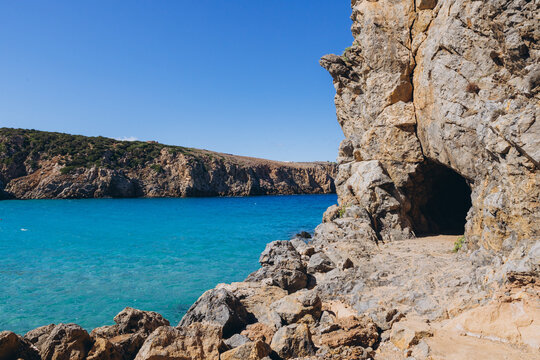 Cala Domestica beach in Buggerru, Italy featuring turquoise Mediterranean sea with rugged rocky cliffs and a cave entrance