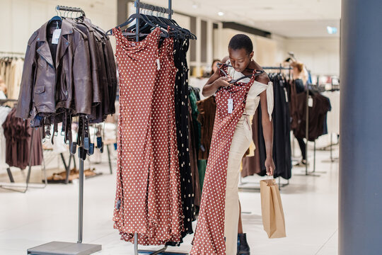 Cheerful African American Woman Holding Stylish Patterned Dress in Apparel Shop