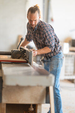 Carpenter planing wood plank using a jointer machine