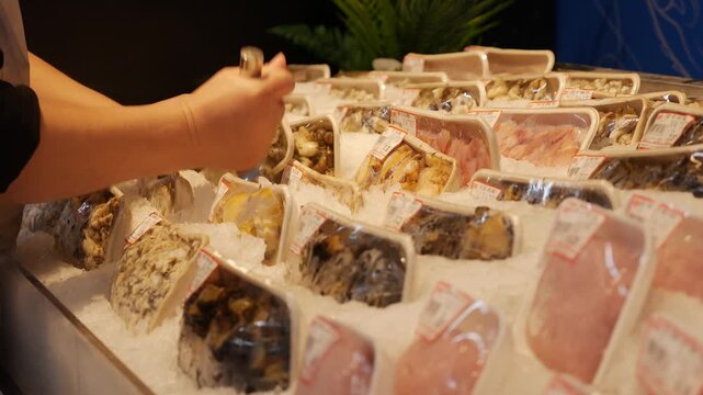 Various packaged seafood products lie on crushed ice in a supermarket display, forming rows of fresh items in refrigerated retail storage. Seafood market.