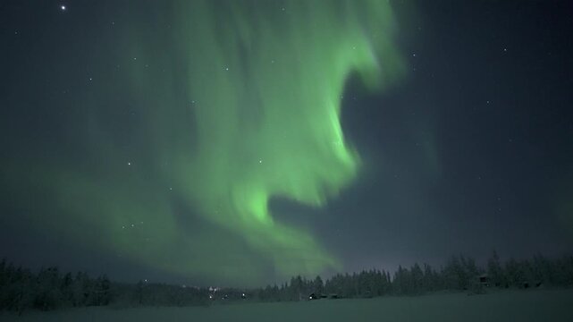 Powerful aurora borealis swirling over snowy forest and cabins, real time