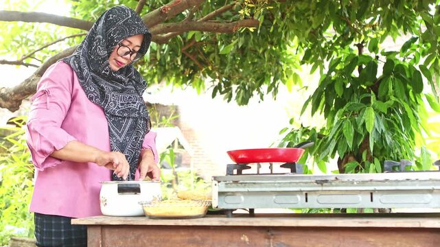 Muslim woman wearing a hijab cooking traditional indonesian food outdoors