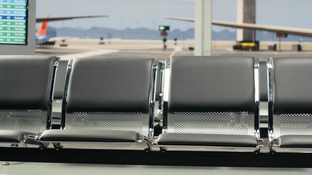 Vacant airport waiting lounge with metal benches and plane runway view on glass windows. Distant control tower in background outside departure hub managing aircraft traffic