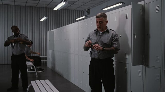 Three Athletic Male Airport Security Officers in Grey Uniforms in Modern Locker Room, Changing Into Civilian Clothes and Chatting, Relaxing After Finishing Work Duty. Concept of Shift Change.