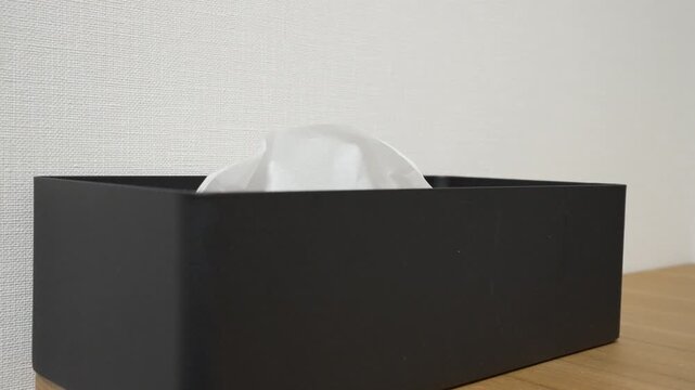 Hand pulling a tissue from black metal tissue box on white background in slow motion, minimal hygiene concept
