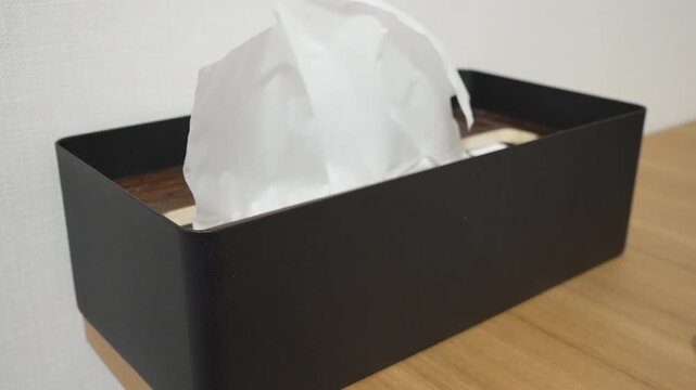 Hand pulling a tissue from black metal tissue box on white background, minimal hygiene concept