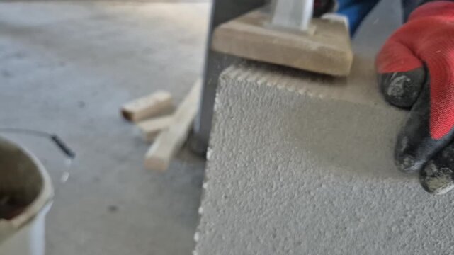 Close up front view of a worker sanding the surface of an aerated concrete block to prepare it for installation.
