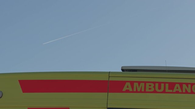 Ambulance under bright sky. Ambulance with flashing blue light under clear blue sky. Emergency ambulance with flashing blue beacon parked beneath bright sunny daytime sky