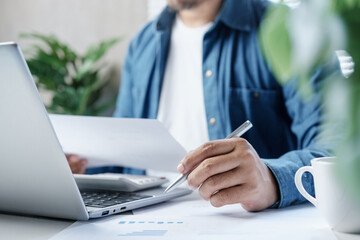 Business professional reviewing financial documents and calculating expenses on laptop with calculator at desk, personal finance management, accounting analysis and budget planning in modern workspace © LAONG