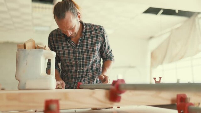 Professional carpenter gluing wood planks together in workshop
