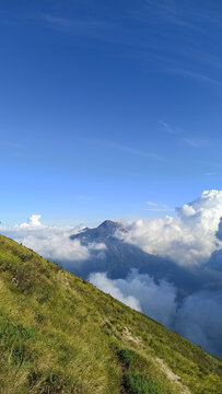 Clear blue sky with scattered white clouds above rolling green hills, creating a fresh and peaceful natural landscape.