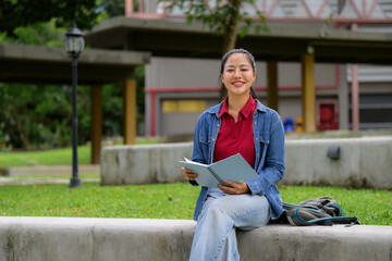 Obraz premium Young Asian student smiling and reading in campus park