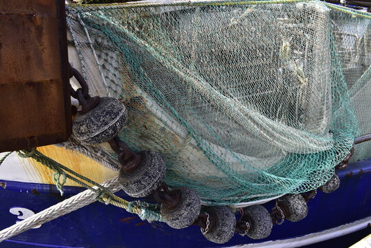 Commercial fishing boat with heavy green trawl net and sinker weights along the hull.