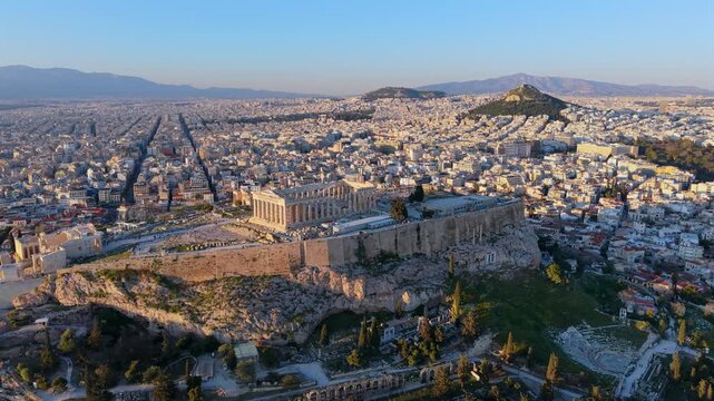 Aerial video of the Acropolis of Athens, the Parthenon, and the Odeon of Herodes Atticus, with the city landscape and mountains during the golden hour.