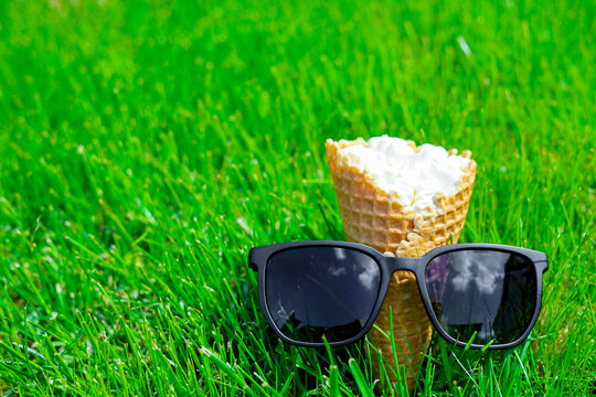 Close up creamy ice cream and sunglasses in a serene lawn setting. Summer vacation concept. Ice cream on bright green grass background. 
