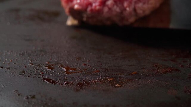 A juicy burger patty being flipped on a hot grill. Spatula flips burgers . 
Chef using spatula to flip large beef burger as. Well done tasty delicious meat cooked outside.