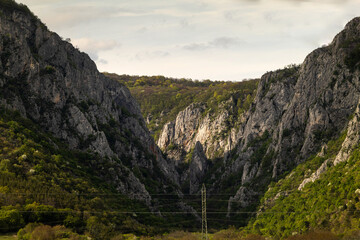 Fototapeta premium Mountains meet in a valley during late afternoon near a power line
